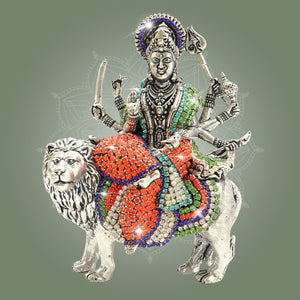 Decorative figurine of a deity on a lion with colorful embellishments on a gray background